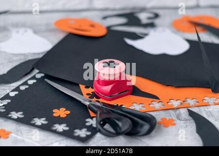 Preparation for Halloween Decoration for the holidays, cutting from colored paper on a white brick wall. orange and black colored paper, scissors, pencils, figured hole punch Soft focus. Stock Photo
