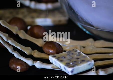 skeletal hands holding spilled chocolates and candies on a black background Stock Photo