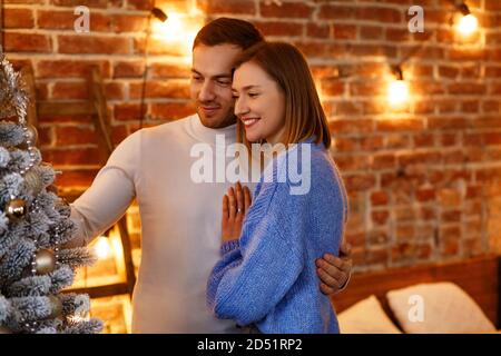 Beautiful young couple at home decorating a Christmas tree. Spending time together, relationships and people concept. Winter holidays, Christmas Stock Photo
