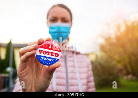 Woman with face mask showing I voted today button at american elections outside. Stock Photo