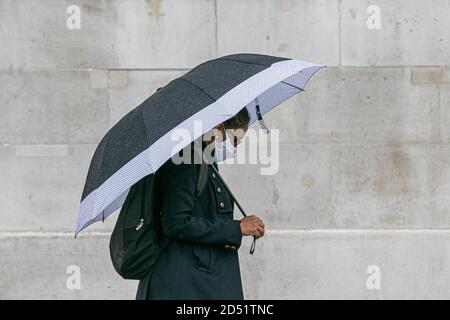 LONDON,UK  12 October 2020. A pedestrian in Trafalgar Square shelters underneath an umbrella during a rain shower. The Met office has forecast several days of rain in the capital.  Credit: amer ghazzal/Alamy Live News Stock Photo