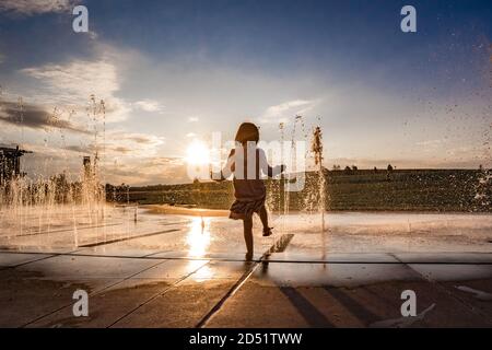 young girl hold her foot in the water at a splash pad at sunset Stock Photo