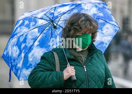 LONDON,UK  12 October 2020. A pedestrian in Trafalgar Square shelters underneath an umbrella during a rain shower. The Met office has forecast several days of rain in the capital.  Credit: amer ghazzal/Alamy Live News Stock Photo