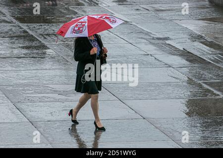 LONDON,UK  12 October 2020. A woman pedestrian in Trafalgar Square shelters underneath an umbrella during a rain shower. The Met office has forecast several days of rain in the capital.  Credit: amer ghazzal/Alamy Live News Stock Photo