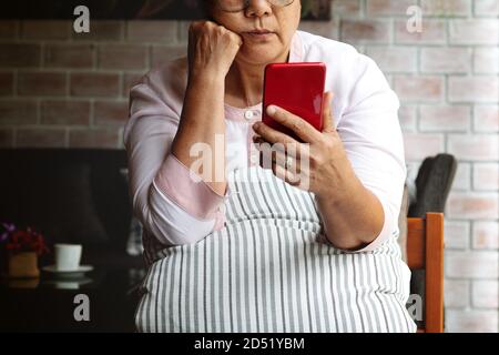 Frustrated older mature woman feeling boring desperate looking on the smartphone, stressed sad middle aged female depressed by hearing bad news Stock Photo