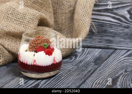 Dessert made from cream cheese with raspberry jelly. Decorated with cookies, raspberries and mint. On pine planks in black. Stock Photo