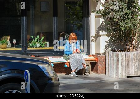 red haired woman outdoors uses mobile phone sitting on the bench, Moscow 28/08/2019 Stock Photo