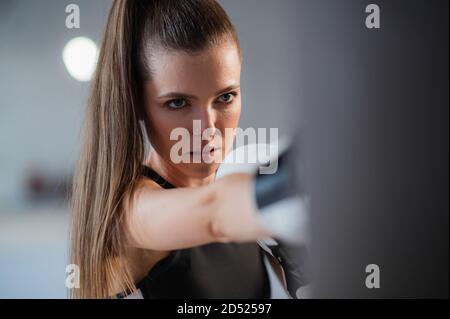 A pretty kickboxer girl is preparing for competitions in the boxing hall, practicing the technique of punches on a punching bag Stock Photo
