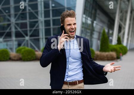 Portrait of handsome smiling man in casual wear holding smartphone. Successful manager makes a call. Young businessman talking on the phone, standing Stock Photo