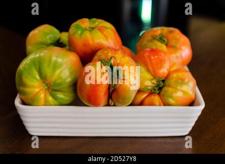 Tomatoes (Solanum lycopersicum, Lycopersicon esculentum) also known as beef or cow heart tomatoes in a white recipient on a wooden table. Selective fo Stock Photo