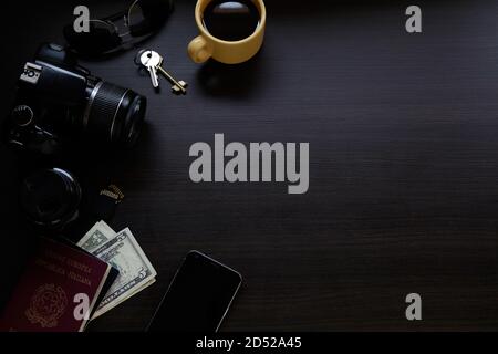Top view of dark wooden desk with reflex digital camera, an smartphone, passport, keys, coffee cup and money. Copy space. Stock Photo