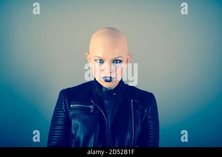 Emotive photo of a beautiful bald woman while standing in the studio and wearing a black leather jacket. Stock Photo