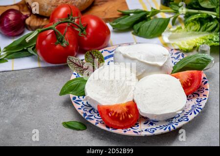 Making of fresh caprese salad with soft Italian cheese from Campania buffalo mozzarella with ripe tomatoes, basil and olive oil close up Stock Photo