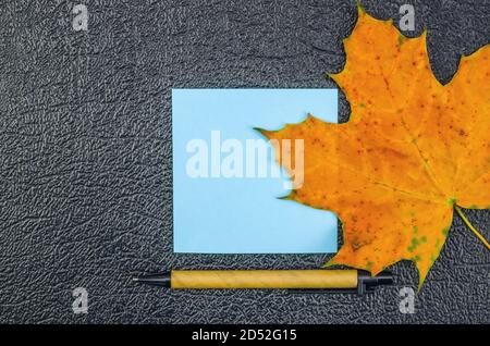 Blue note sheet with maple leaf and pen on a dark background with space for text, top view. Beautiful background for notes, top view Stock Photo