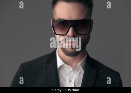 Closeup of confident fashion model wearing suit and sunglasses while standing on gray studio background Stock Photo