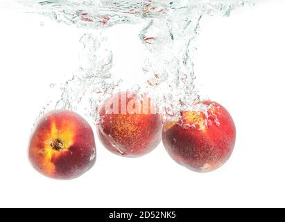 Three peaches falling into water with splash Stock Photo