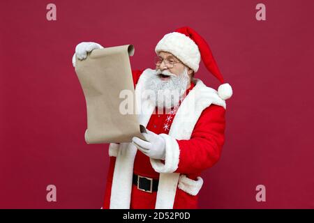 Happy Santa Claus reading wish list isolated on red background. Stock Photo