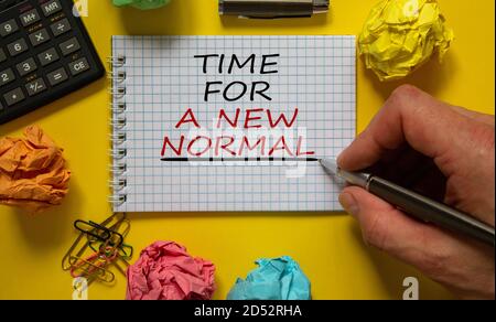 Mail hand writing 'time for a new normal' on white note, beautiful yellow background, colored paper clips, metalic pen, cap and calculator. Business c Stock Photo