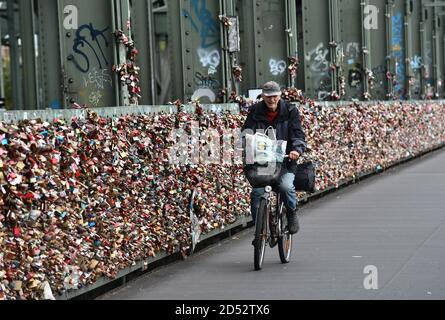 Cologne, Germany, 2020. Man riding bicycle passed thousands of love locks on The Hohenzollern Bridge crossing the River Rhine Hohenzollernbrücke Stock Photo