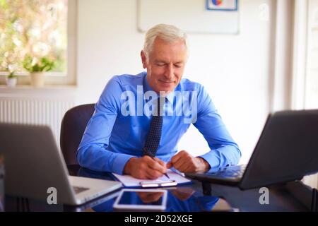 Smiling senior businessman doing some paperwork while sitting at office desk and working on presentation. Stock Photo