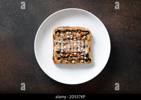Crispy sandwich with peanut paste in white plate isolated on brown background. Healthy breakfast. View from above. Stock Photo