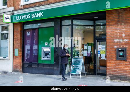 A man wearing a mask waits outside a branch of Lloyds Bank to observe social distancing rules, Grays Inn Road, King's Cross, London, UK Stock Photo