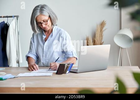 Mature stylish woman fashion designer drawing sketches in modern studio. Stock Photo