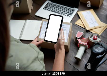 Female warehouse worker holding parcel box using mobile app on smartphone. Stock Photo