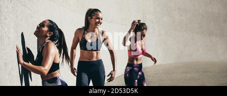 Female friends taking break after workout session outdoors. Three young woman relaxing after physical training session in morning. Stock Photo