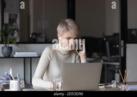 Smiling businesswoman work on computer talking on cell Stock Photo