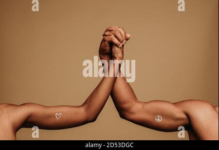 Close up of hands of man and woman holding each other showing unity and togetherness. Cropped shot of two arms together with symbols associated with b Stock Photo