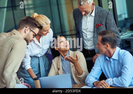 Group of multiracial business people in classic wear looking at laptop screen and discussing new project while working together in the modern office Stock Photo