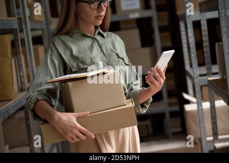 Female warehouse worker holding parcel boxes using mobile application. Stock Photo