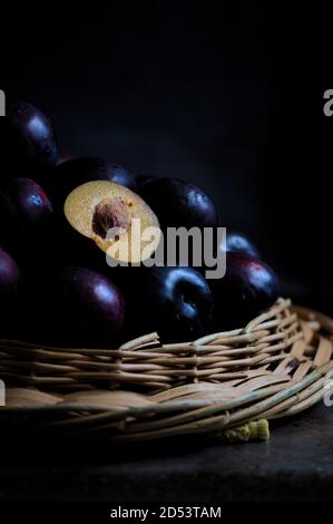 Vertical image of a pile of black plums, among which one half of them stands out on a dark background in the style of dark food and with copy space. Stock Photo