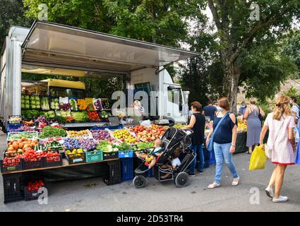 Glimpse of the weekly city market in Viale Macchi, with women buying fresh fruits and vegetables from a food stall in summer, Siena, Tuscany, Italy