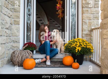 Woman and her dog sitting in doorway of home decorated for fall. Stock Photo