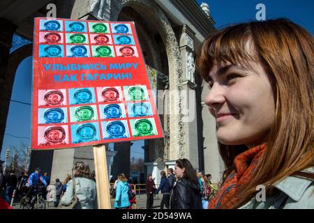 Russia, Moscow, 12th of April 2015: Participants in the Star Parade hold portraits of the first cosmonaut Yuri Gagarin on Cosmonautics Day march by the central alley at the Exhibition of Achievements of the National Economy in Moscow. A woman holds a banner which reads "Smile at the world like Gagarin" Stock Photo