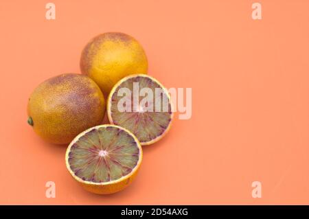 Close-up of a group of blood oranges, one of which is split into two parts to appreciate the reddish color inside. All on orange background with copy Stock Photo