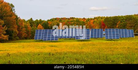 rural farm field harvesting the energy from the sun with solar panels  with trees in fall foliage colors in the background Stock Photo