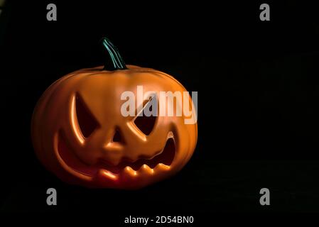 Ghostly isolated plastic Halloween orange pumpkin with scary face on black background with copy space Stock Photo