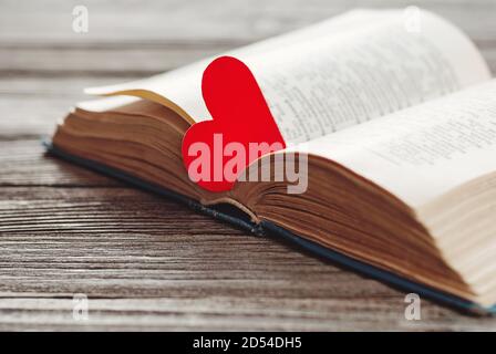 open book with red heart shaped paper bookmark on wooden background Stock Photo