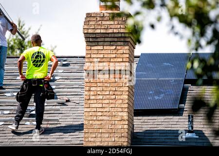 Herndon, USA - August 27, 2020: Man worker installing working on rooftop solar panels mounted on racking racks and rails on top of house residential h Stock Photo