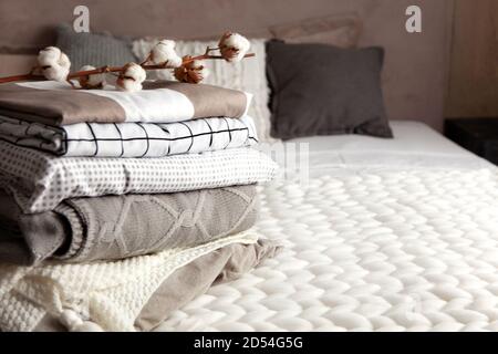 Stack of folded warm blankets with different design patterns and cotton branch on grey background Stock Photo