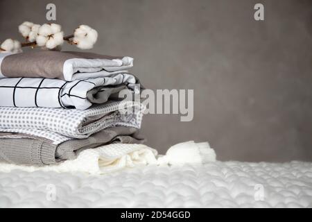 Stack of folded warm blankets with different design patterns and cotton branch on grey background Stock Photo