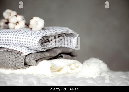 Stack of folded warm blankets with different design patterns and cotton branch on grey background Stock Photo