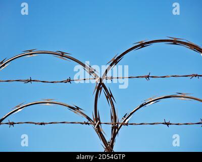 Close-Up Of Razor Wire and Barbed Wire against blue sky Stock Photo