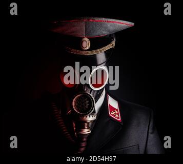 Portrait photo of a post apocalyptic military officer in uniform suit and peaked cap standing in soviet gas mask on black background. Stock Photo