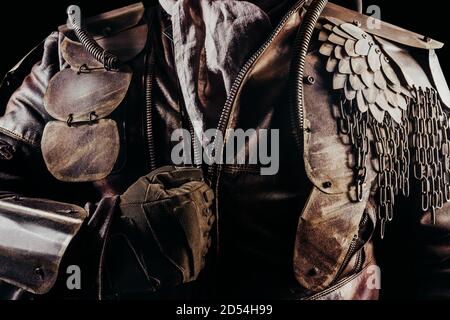 Photo of a post apocalyptic raider warrior putting on leather jacket with metal armor on black background. Stock Photo