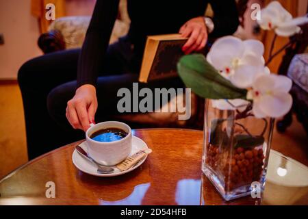 Selective focus shot of a woman drinking coffee while reading a book Stock Photo