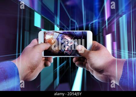 First person view photo of a male hand in jeans shirt holding smartphone and playing futuristic shooter game on neon evirontment background. Stock Photo